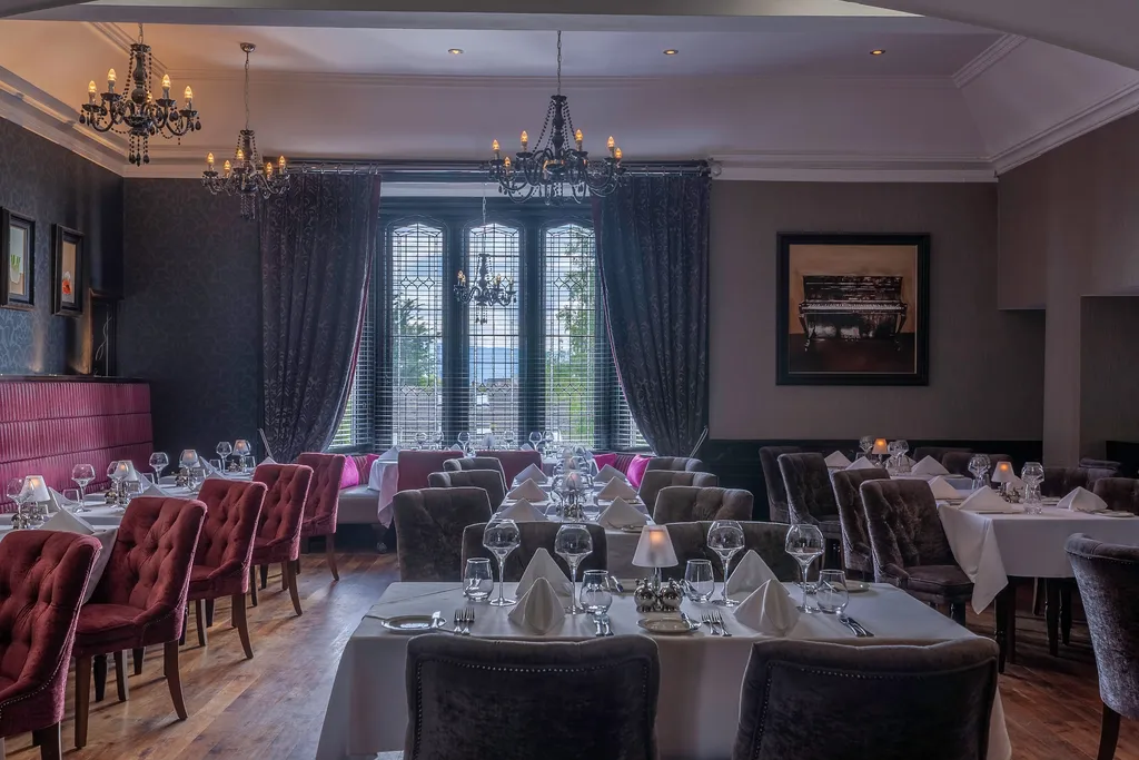 Fahrenheit Restaurant's dining room with black chandeliers, a stained-glass window, and burgundy velvet chairs