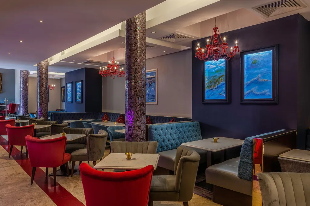 Indigo Lounge seating with red velvet armchairs, tufted blue banquettes, mosaic pillars, and red crystal chandeliers
