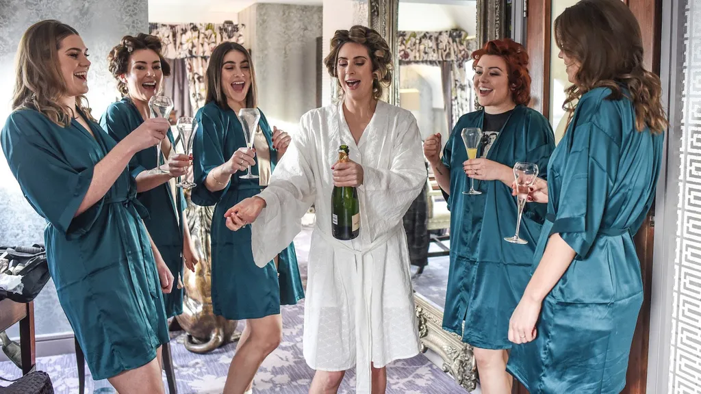 Bridesmaids in teal robes toasting with champagne
