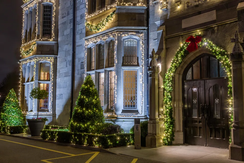 The castle’s arched front doorway framed by a garland with a red bow, beside bay windows and conical trees lit with fairy lights