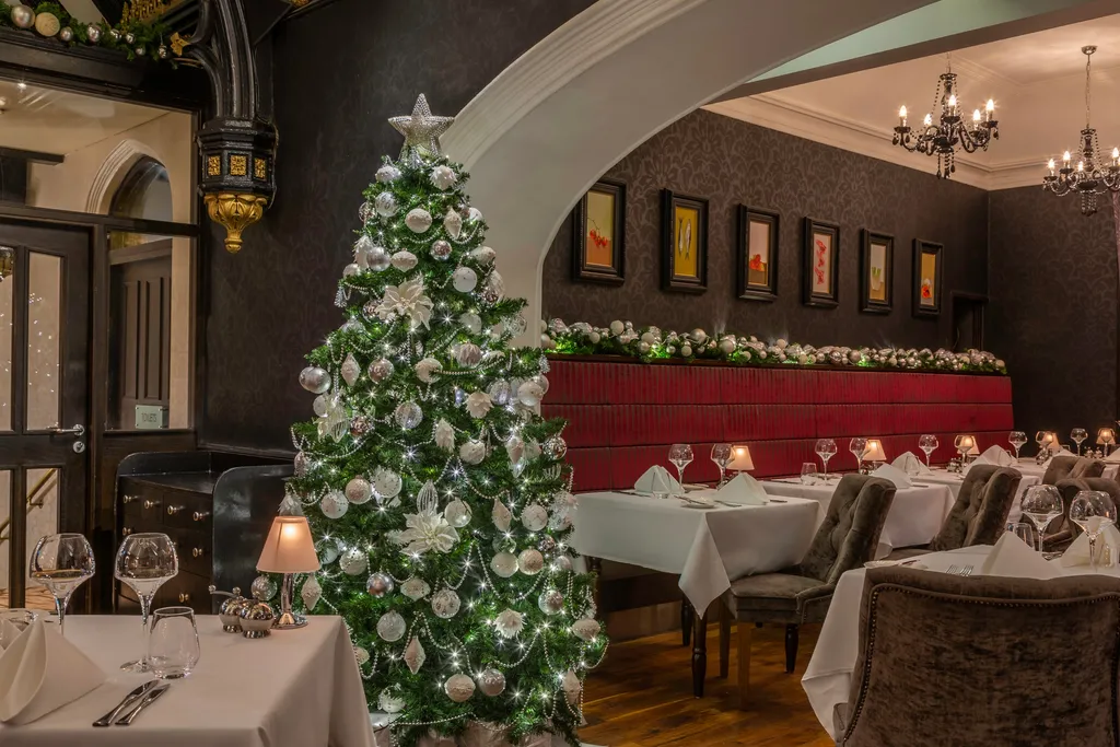 A Christmas tree with silver and white baubles in Fahrenheit Restaurant, beside the red banquette and tables set for dinner