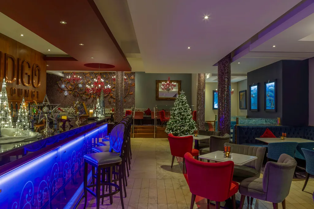 Indigo Lounge at Christmas, its blue-lit bar lined with festive trees and a tall Christmas tree in the lounge beyond