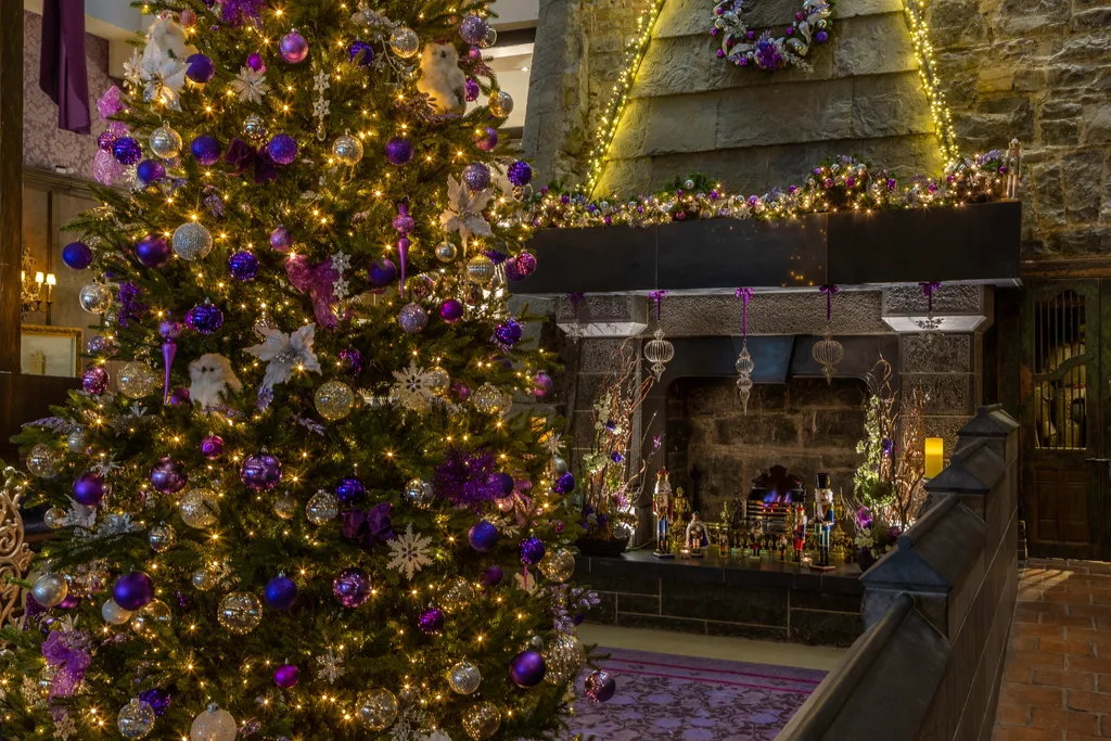 A Christmas tree trimmed with purple and gold ornaments before the lobby’s stone fireplace and its lit garland