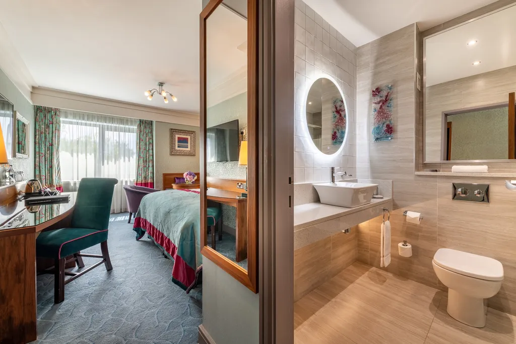 Deluxe Room seen past the open bathroom door, with a backlit mirror and basin and the bedroom beyond