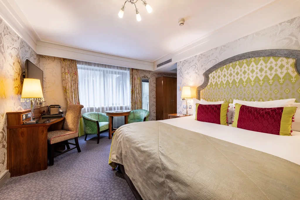 Executive Double Room king bed with a lime patterned headboard, desk and armchairs by the window