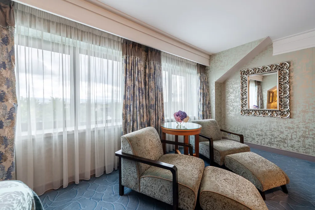Executive Family Room lounge area with armchairs, a footstool and a round table by tall windows