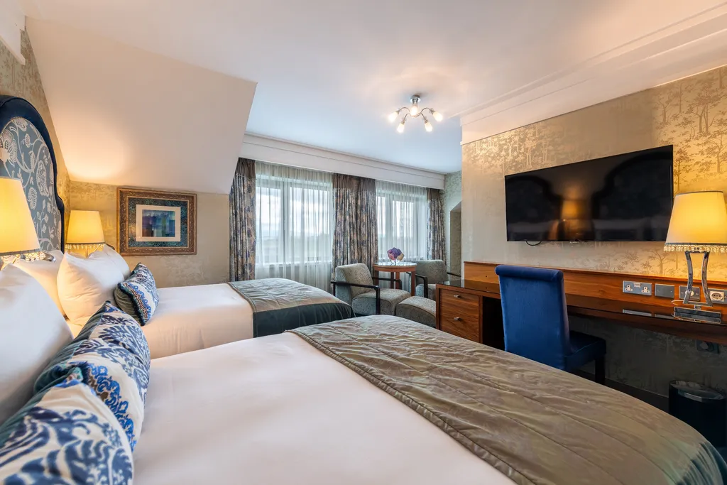 Executive Family Room with two beds, blue floral cushions, a desk and wall-mounted TV