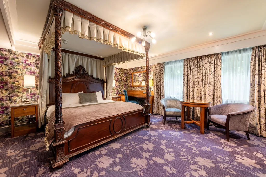 Executive Four-Poster Room with a carved four-poster bed, armchairs by the window and floral wallpaper