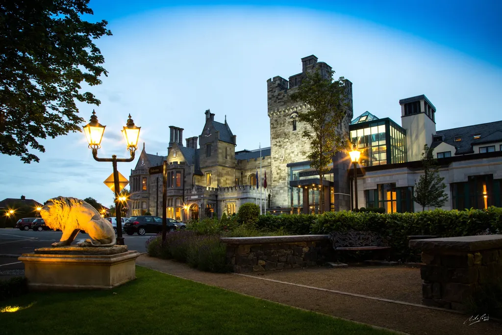 Lamp-lit lawn and a stone lion, the castle behind at dusk
