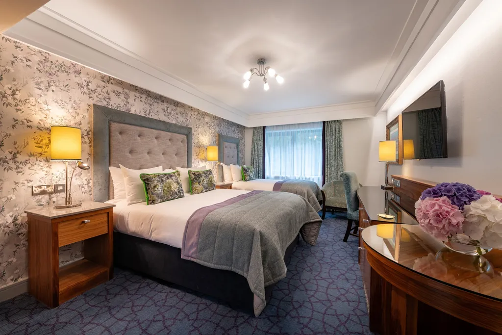 Family Room with two beds, a round table with hydrangeas and floral wallpaper