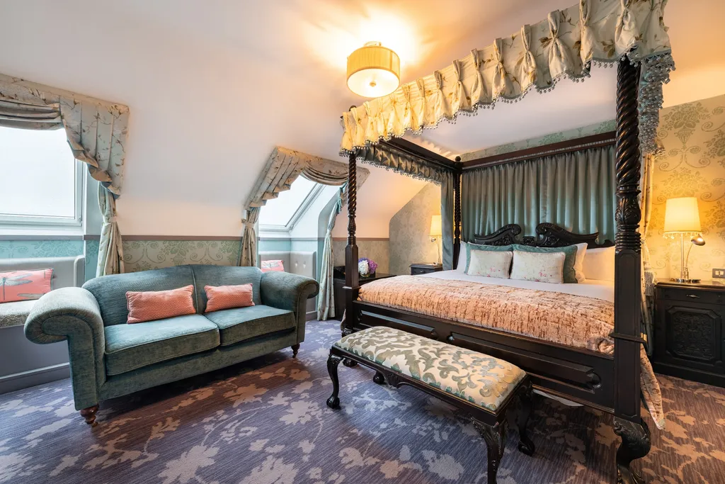 Junior Suite seating area with a teal sofa beside the four-poster bed