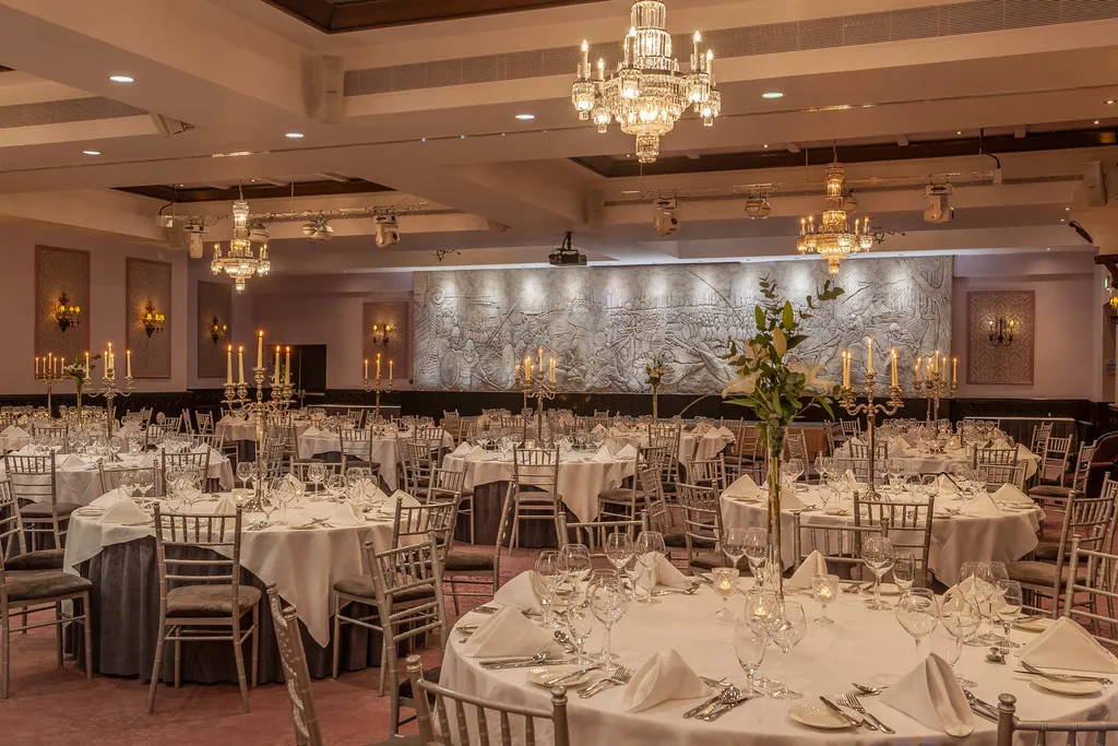 The Great Hall laid for a banquet with round tables, candelabra and crystal chandeliers, the Battle of Clontarf frieze lit along the far wall