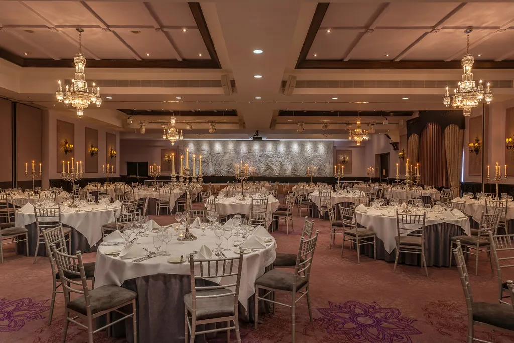 A wide view of the Great Hall set for a gala dinner, with candelabra on every table and the carved frieze at the far end