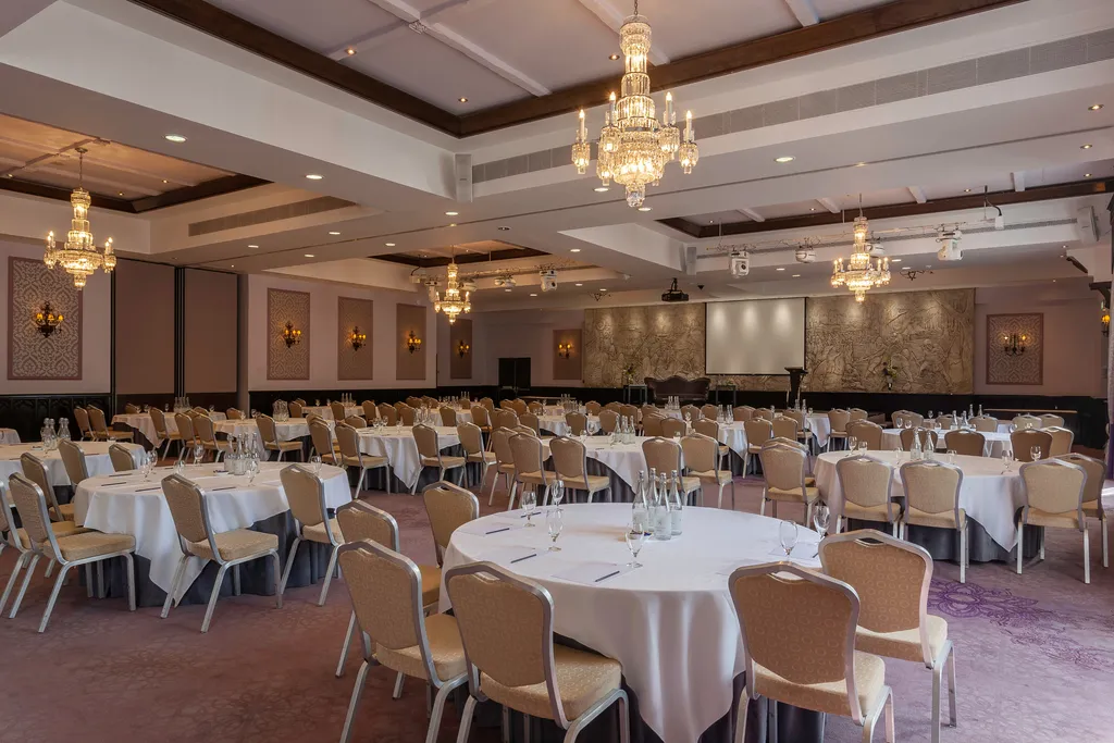 The Great Hall set cabaret style for a large conference, with rows of round tables facing a projector screen and the carved frieze