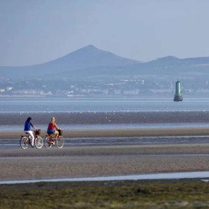 Two cyclists on the beach at Dublin Bay with mountains beyond