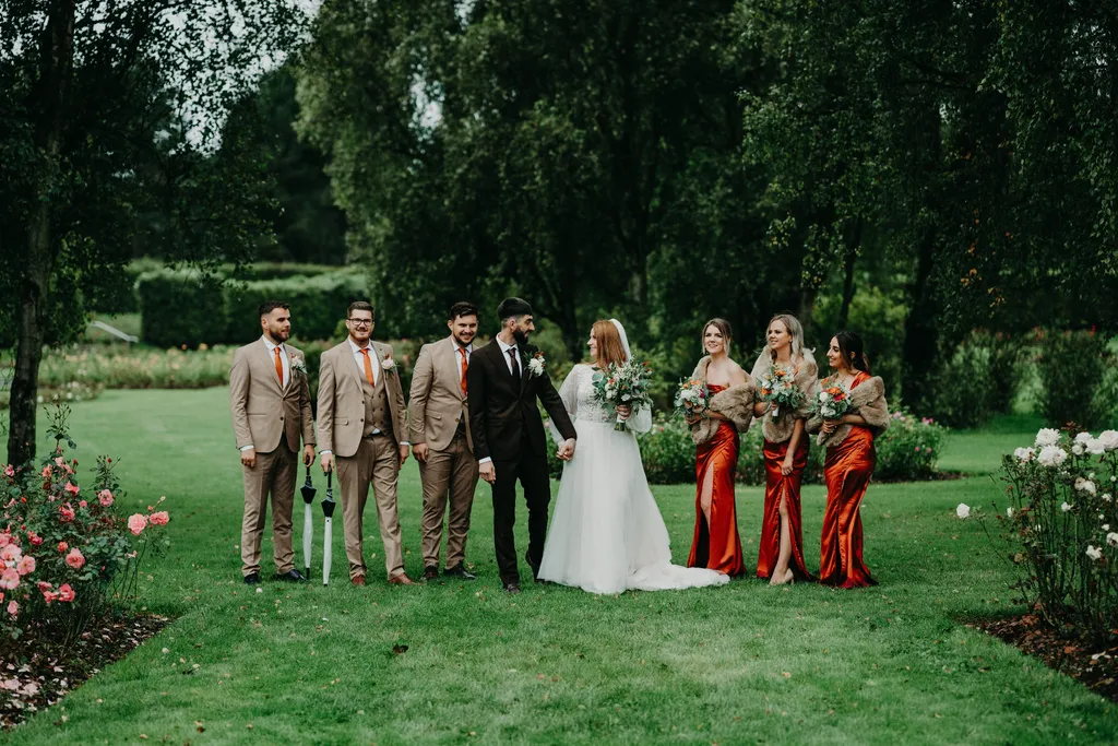 A bride and groom with groomsmen in beige suits and bridesmaids in rust satin dresses on the castle lawn