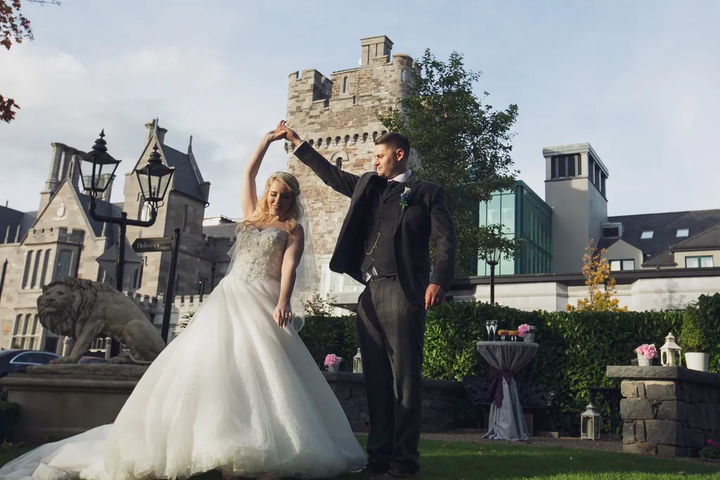 A groom twirling his bride in a full ballgown on the castle lawn, with the stone tower and gatehouse behind